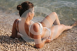Sexy woman in bikini on the beach enjoying summer sun. Beautiful woman lies near the sea. Water wets her feet