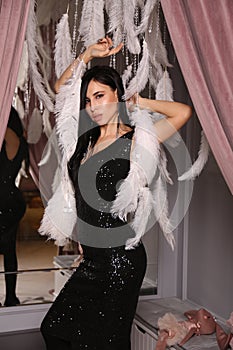 Sexy woman with dark hair in elegant black dress posing with decorations from feathers