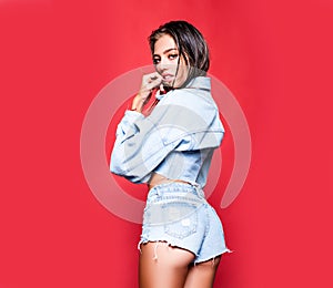 Sexy woman in the fashion jeans dress isolated on red.