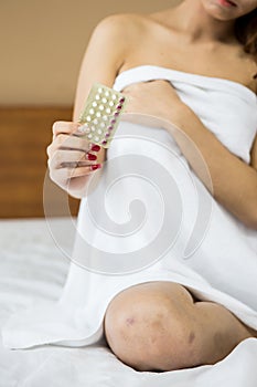 woman holding birth-control pill on bed in bedroom