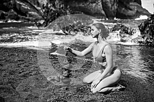 Sexy woman making stack of pebbles stone against sea background for spa, balance, meditation and zen theme. Life balance