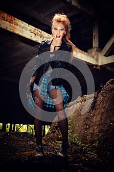 Sexy woman model in leather bib and plaid grunge style shirt in ripped mesh pantyhose with blonde hair with Mohawk and