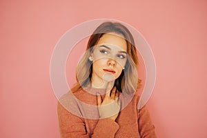 Sexy woman in a pink sweater isolated on a pink background, pensively looking away with a serious face. Copy space
