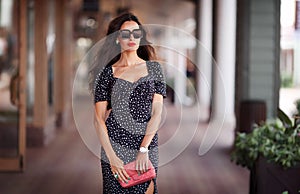 Sexy woman portrait, Caucasian beautiful trend female posing near window of clothing store, holding handbag, wearing dress and