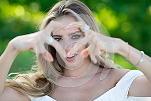 Sexy woman with sensual look with love heart finger in spring park. Beauty portrait of beautiful female model outside