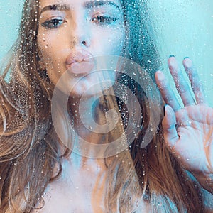 woman in shower. Attractive young naked woman under water drops on blue background