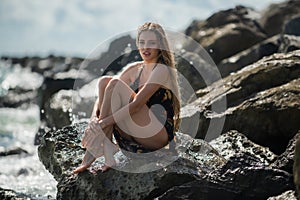Sexy woman sit on stone rocks on beach. Traveller woman summer dress on beautiful sandy beach. Cute girl enjoy her
