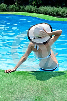 woman in sun hat relaxing in the pool, rear view.