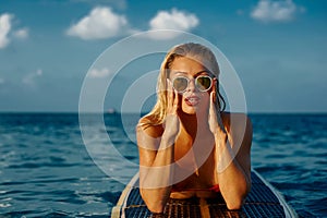 Sexy woman in sunglasses posing, lying on a longboard in the sea