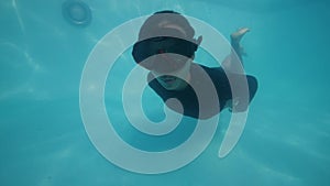 Sexy woman swimming underwater in a pool showing toungue and making peace sign. Active and happy woman concept.