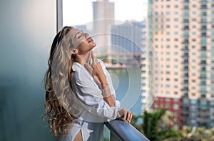 Sexy woman on terrace. Young lady in stylish shirt poses on balcony and enjoys spring. Girl on terraced house by the sea