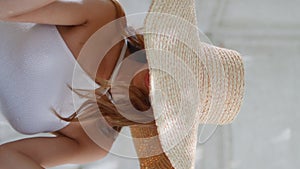 Sexy woman touching straw hat posing with gentle smile at sunlight cafe vertical