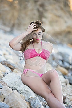 woman wear pink bikini sitting on sea rocks