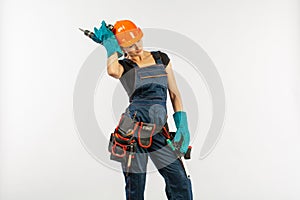 workwoman in overalls and safety helmet with tool belt holding electric drill, on white background