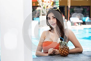 Sexy young asian woman in swimsuits in summer. beautiful woman in orange bikini with hat and tropical drink in swimming pool