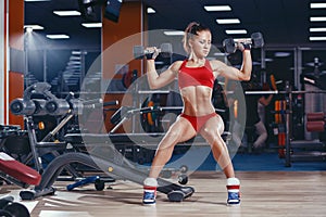 young athletics girl doing dumbbells press exercises sitting on bench in gym