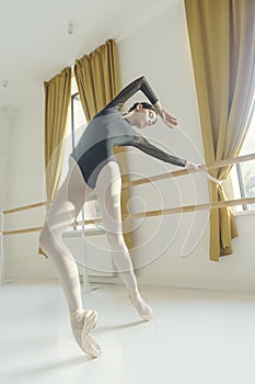 sexy young ballerina standing in a deflection at the ballet machine leaning on it with her hands