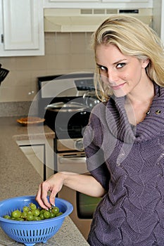 young blonde woman washing grapes in kitchen