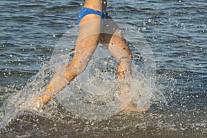 A young brunette woman or girl wearing a bikini running through the surf on a deserted tropical beach with a blue sky. Young