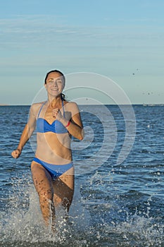 A young brunette woman or girl wearing a bikini running through the surf on a deserted tropical beach with a blue sky. Young