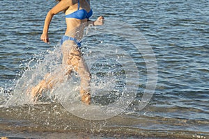 A sexy young brunette woman or girl wearing a bikini running through the surf on a deserted tropical beach with a blue sky. Young