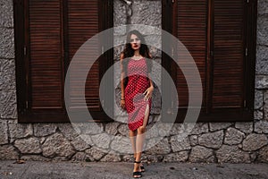 Sexy young Caucasian girl in red dress posing on beautiful historical street in Europe