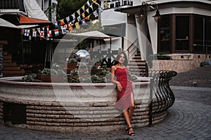 Sexy young Caucasian girl in red dress posing on beautiful historical street in Europe