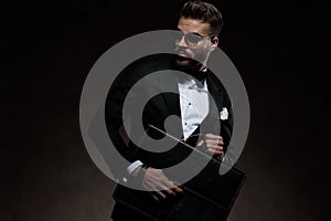 Sexy young elegant man in tuxedo holds and opens briefcase