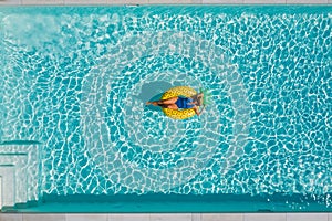 Sexy young female in swimsuit bikini, in a straw hat and sunglasses floating on blue swimming pool waves on giant inflatable