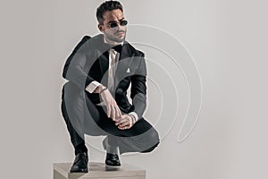 Sexy young groom in elegant tuxedo with glasses looking away and crouching