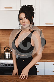 Sexy young Latino woman with big breasts in a black sexy outfit looking in camera and posing in the kitchen. Busty model photo