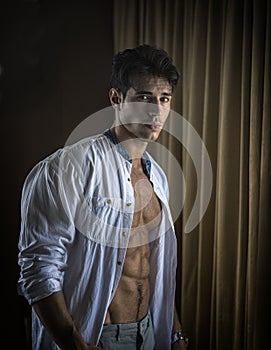 Sexy young man dressing by window curtains