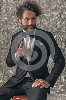 Sexy young man in elegant tuxedo looking to side and fixing jacket