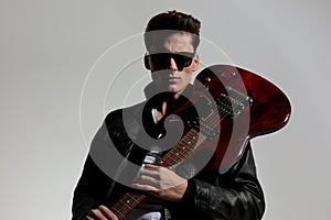 sexy young man with glasses wearing guitar on his shoulder and posing