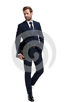 Sexy young man in navy blue suit holding suitcase in fashion pose