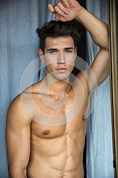 young man standing shirtless by curtains