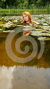 Sexy young redhead woman mermaid swims plays sensitively seductive with pink water lilies in the water, with reflection