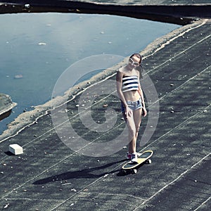 Sexy young trendy girl with skateboard posing on the roof