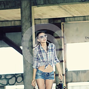 Sexy young trendy girl with skateboard posing on the roof