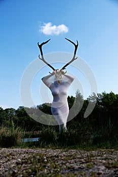 sexy young woman in a big transparent stocking dress with voluptuous curves holding a deer skull with deer antlers in front