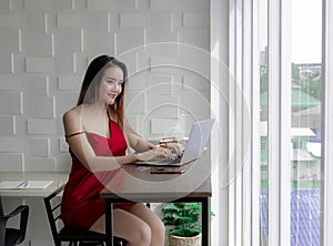 Sexy young woman in a red dress. With a comfortable holiday. The living room is checking work on Notebook. View emails for