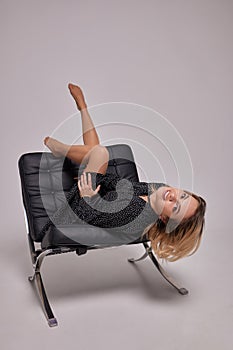 A sexy young woman in a shirt and hat is sitting on a black leather sofa.