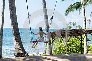 young woman sitting on the swing on the tropical beach, paradise island Bali, Indonesia. Sunny day, happy vacation