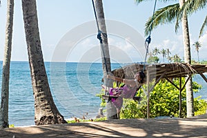 young woman sitting on the swing on the tropical beach, paradise island Bali, Indonesia. Sunny day, happy vacation