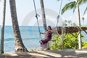 young woman sitting on the swing on the tropical beach, paradise island Bali, Indonesia. Sunny day, happy vacation