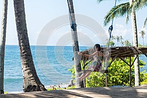 young woman sitting on the swing on the tropical beach, paradise island Bali, Indonesia. Sunny day, happy vacation