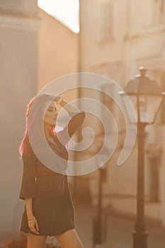 Sexy young woman with a slim perfect body and pink hair in a short dress walking on the street at the sunset. Fashion