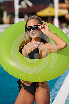 Sexy young woman in swimming suit holding inflatable ring near pool.