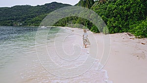 Seychelles. Drone aerial follows young woman running along the paradise beach with palm trees at Mahe island. Travel