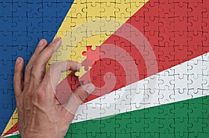 Seychelles flag is depicted on a puzzle, which the man`s hand completes to fold